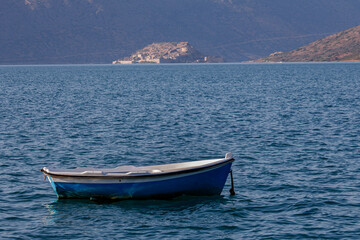 Small blue boat floating on clear sea waters with scenic view of historic Spinalonga fortress island in Elounda, Crete. © Bill Lezos