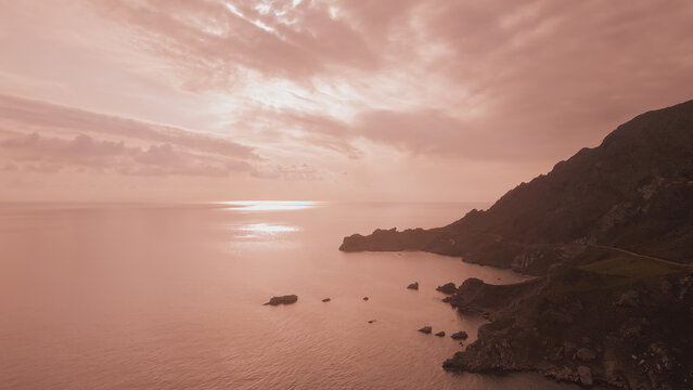 Aerial panoramic view of rocky sea coast and dark cliff silhouette under hazy pink sunset light in Greece for mysterious dramatic landscape background