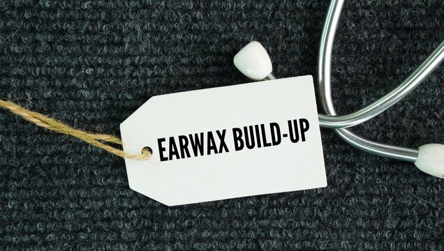 Stethoscope and paper tag with the word Earwax buildup occurs when cerumen -earwax- accumulates faster than the ear can naturally clear it, often worsened by using cotton swabs.