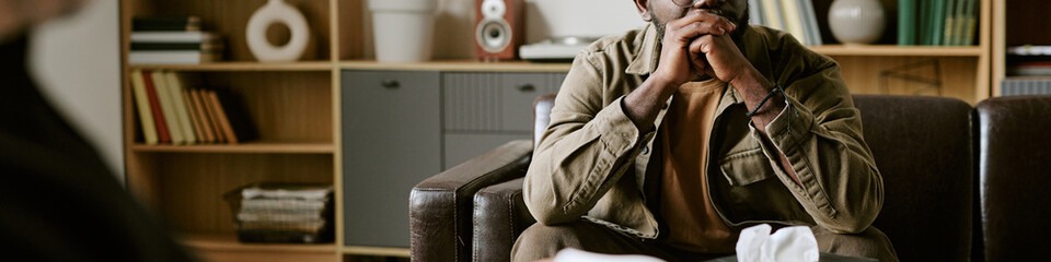 Header of middle aged African American man sitting on couch during therapy session in psychology office. Image represents mental health counseling for healthcare campaigns