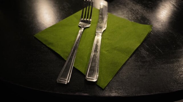 Dirty cutlery with stains on black cafe table. Fork and knife on green napkin in cheap unhygienic cafe. Unsanitary restaurant table setting with smudged metal utensils under indoor lighting