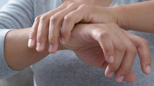 pain in hands and joints. woman feeling hand discomfort, rubbing and massaging wrist and fingers, performing warm-up exercises to alleviate pain, carpal tunnel syndrome, arthritis, or cramp symptoms.