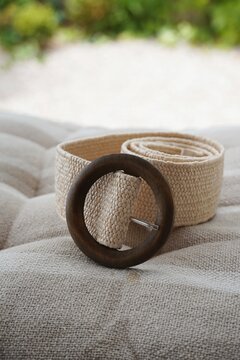 Woven raffia straw belt with round wooden buckle on beige linen fabric