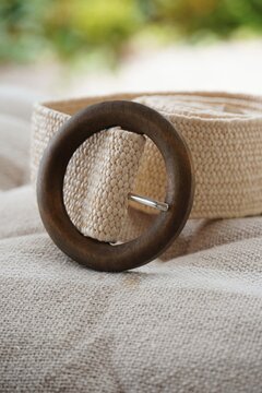 Woven raffia straw belt with round wooden buckle on beige linen fabric