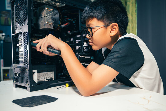 Young boy concentrating while repairing and assembling hardware inside an open desktop computer case at home, learning technology and problem solving skills