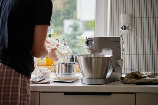 Woman pours flour into a sifter beside a stand mixer on the kitchen counter
