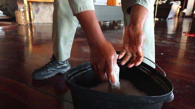Worker wrings a soapy cloth into a bucket during routine maintenance