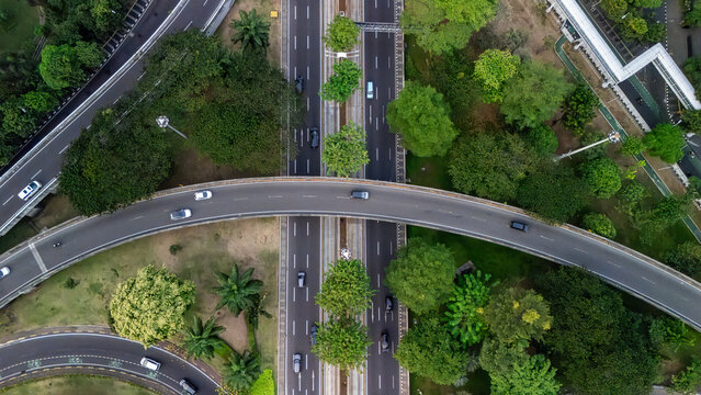 Aerial view of a highway interchange surrounded by lush green trees and urban landscaping in Jakarta, Indonesia.