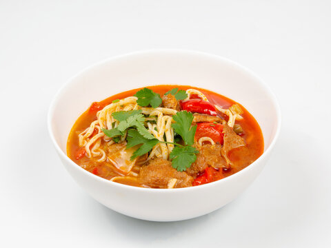 Hot spicy soup with noodles, meat, vegetables, and fresh herbs in a white bowl