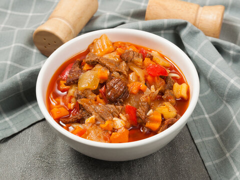 Rich beef stew and vegetable soup with meat chunks, potatoes, carrots, and bell peppers in a white bowl