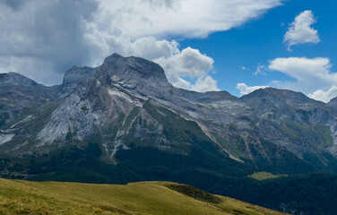 Fototapeta premium serene mountain peak standing majestically in a rocky terrain with lush vegetation under a blue sky and white clouds, viewed from a lower vantage point, travel and nature-themed.