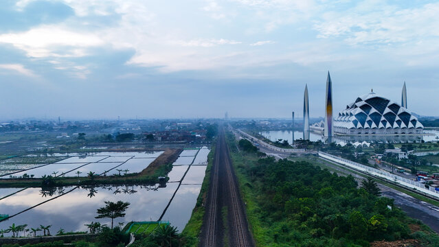 Aerial view of Al Jabbar Grand Mosque surrounded by rice fields and railway tracks in Bandung, West Java, Indonesia.