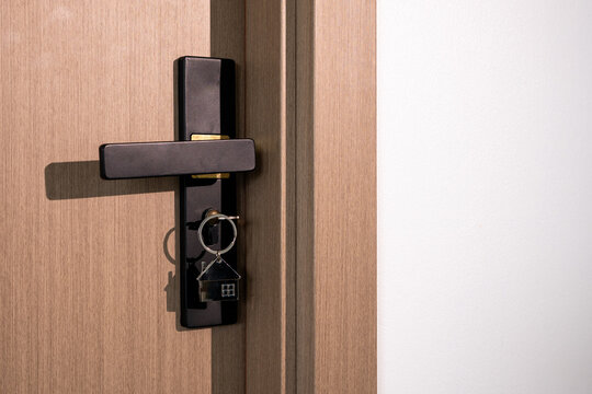 House key with home shaped keychain hanging from a modern door lock, symbolizing home ownership, new property purchase, real estate, moving, security and access to a new residence.