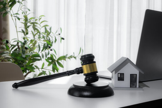 Judge gavel beside a model house and laptop represents real estate law, property auction, mortgage foreclosure, housing contracts, legal disputes and residential property investment in a modern office
