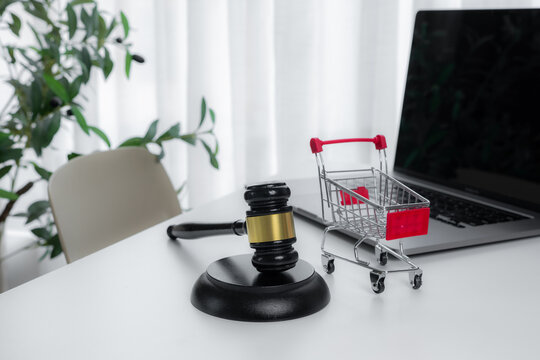 Judge gavel beside shopping cart and laptop symbolizes online auction, digital bidding, ecommerce transactions, consumer law, marketplace disputes, purchasing regulations and commercial justice.
