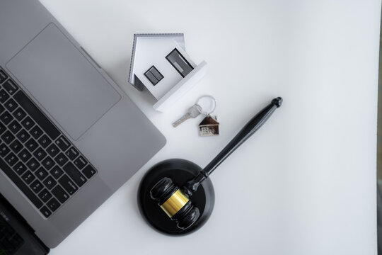 House model, home key, judge gavel and laptop represent home purchase, property ownership, real estate law, legal closing, mortgage contracts and secure residential transactions.