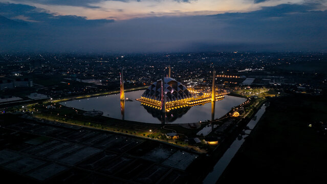 Aerial view of Al Jabbar Grand Mosque illuminated at night, surrounded by a reflective pool with city lights in the background in Bandung, West Java, Indonesia.