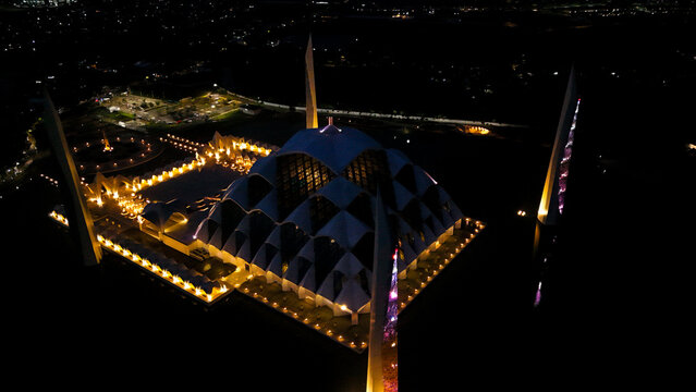 Aerial view of Al Jabbar Grand Mosque illuminated at night with its modern geometric architecture and reflection in the surrounding water in Bandung, West Java, Indonesia.