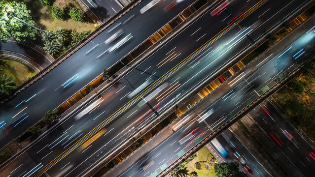 Aerial view of a multi-level highway interchange at night with light trails from moving vehicles in Jakarta, Indonesia.