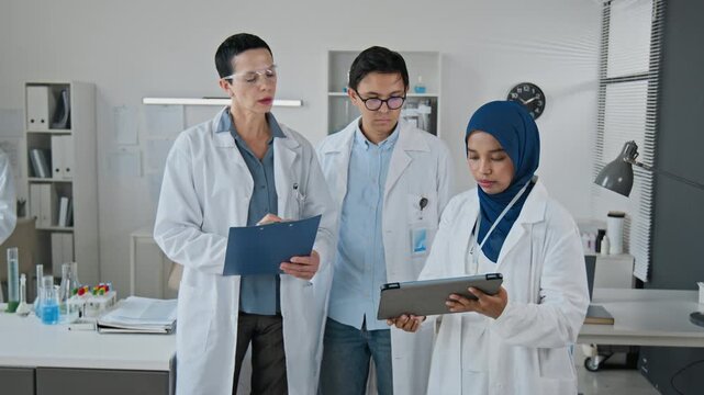 Diverse team of middle aged Caucasian and young adult Asian scientists analyzing data on tablet. Clip works for pharmaceutical research and biotechnology promotional video
