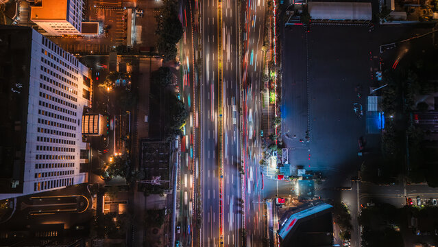 Aerial view of nighttime traffic light trails on a busy highway surrounded by city buildings and urban infrastructure in Jakarta, Indonesia.