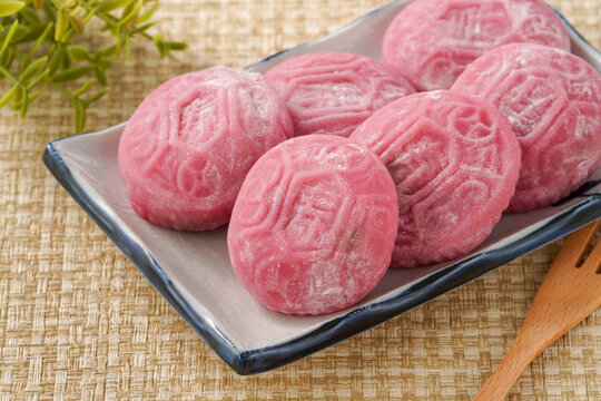 Traditional pink red turtle rice cake on woven grass mat background.