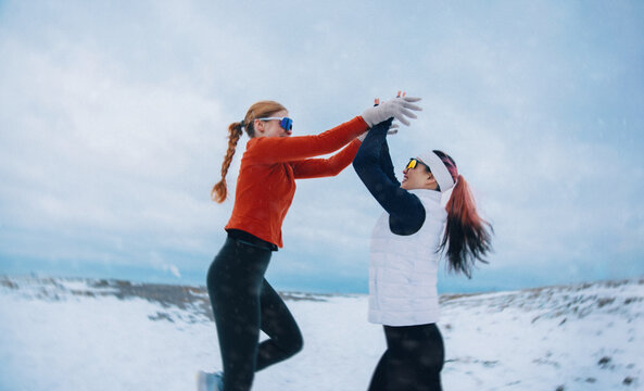 Women celebrating winter running achievement with a high five in the snow