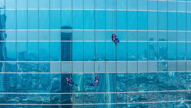 Aerial view of window cleaners suspended on ropes cleaning the glass facade of a modern skyscraper in Jakarta, Indonesia.