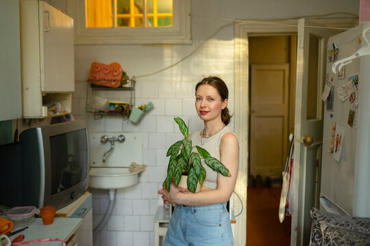 A woman holds a potted plant in her kitchen