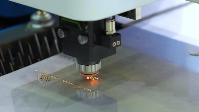 Industrial laser cutting machine etching text on steel plate with orange sparks and high precision movement.