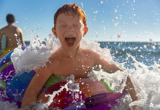 Red-haired boy laughs while swimming with an inflatable in the sea