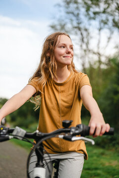 A smiling teenage girl rides a bicycle in the countryside