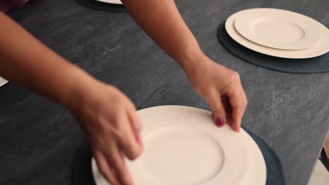 Housekeeper hands arrange white dinner plates on woven placemats at home