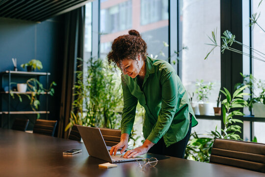 Smiling businesswoman standing at office desk typing on laptop