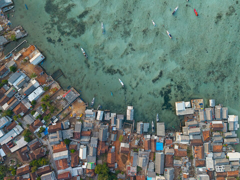 Aerial view of Karimunjawa Village featuring traditional houses, rooftops, and small boats floating in clear turquoise water in Karimunjawa, Central Java, Indonesia.