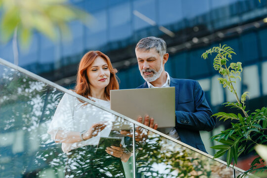 Businessman and businesswoman discuss work on a laptop outdoors