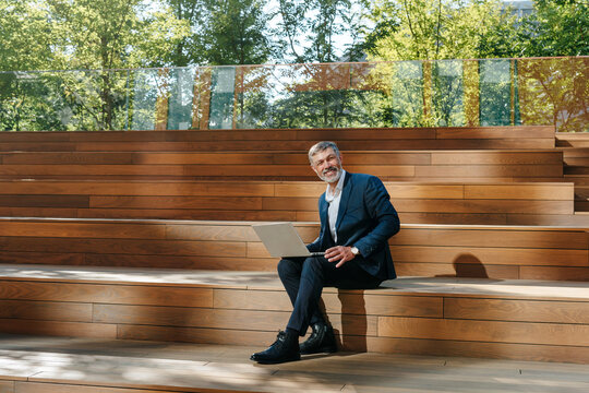 Smiling businessman works on laptop at outdoor wooden amphitheater