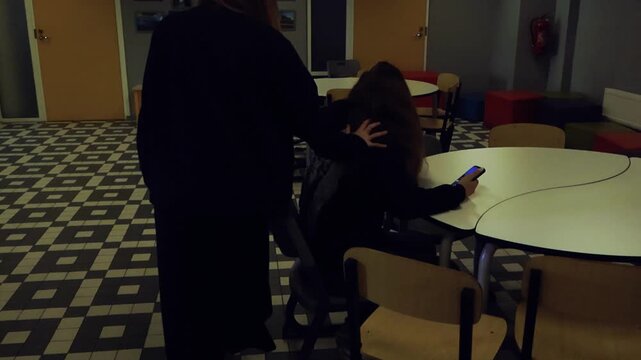 Bully pushing another student in a dark school hallway while other student is scrolling her phone alone
