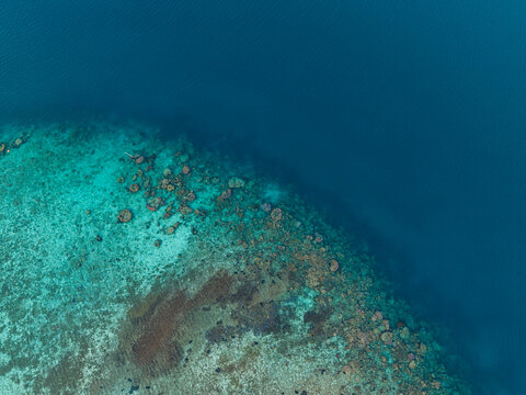 Aerial view of a vibrant coral reef with clear turquoise shallow water transitioning into deep blue ocean depths in Karimunjawa, Central Java, Indonesia.