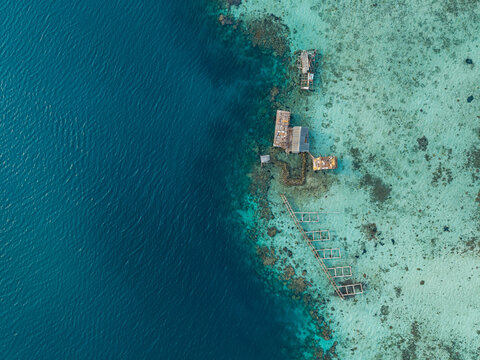 Aerial view of a fish cage situated in the clear turquoise waters of a coral reef with a transition to deep blue sea in Karimunjawa, Central Java, Indonesia.