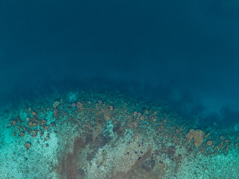 Aerial view of a vibrant coral reef with clear turquoise waters transitioning into deep blue sea in Karimunjawa, Central Java, Indonesia.
