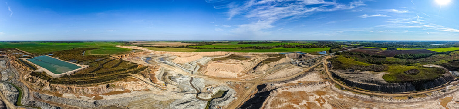 Aerial view of the Dolomitas quarry featuring large excavated pits, sediment ponds, and surrounding green fields under a clear blue sky in Petrasiunai, Siauliu apskritis, Lithuania.
