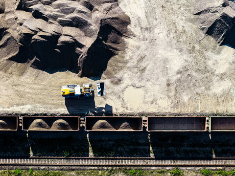 Aerial view of a yellow loader working in a dolomite quarry, loading gravel into train cars on a railway track, with piles of crushed stone in Petrasiunai, Siauliu apskritis, Lithuania.