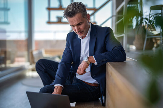 A businessman works on a laptop on the floor in a relaxed office