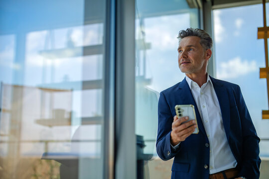 Businessman holds smartphone and looks out office window