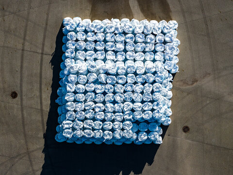 Aerial view of a large stack of white plastic-wrapped agricultural bales arranged on a concrete surface in Latvia.