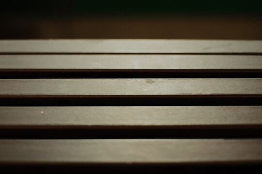 Close up of horizontal wooden slats on bench surface with soft lighting
