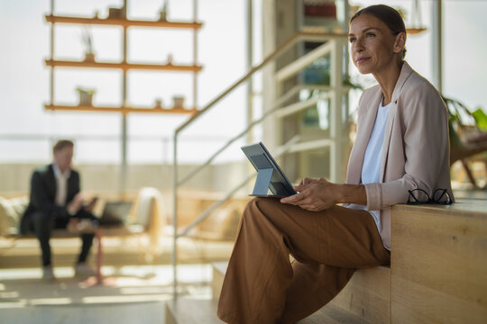Mature businesswoman uses tablet on office staircase with colleague