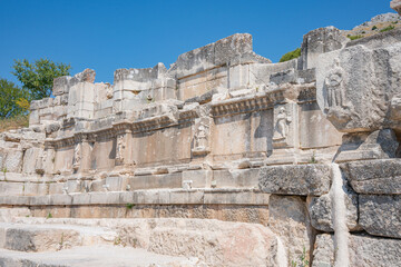 Robed human reliefs line a long decorated stone wall. Carved figures and decorative borders line an ancient stone facade at Sagalassos © Ensar