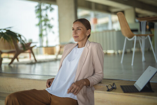 Businesswoman relaxes on staircase with laptop in modern office
